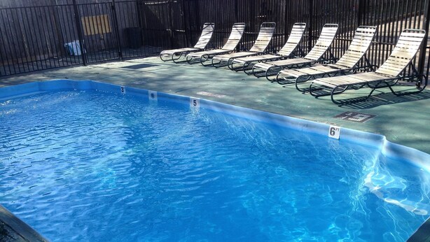 Une piscine rectangulaire à l’eau d’un bleu limpide, entourée d’une clôture en métal noir. Des chaises longues sont alignées le long de la clôture.