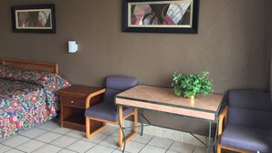 Une chambre d’hôtel avec un lit, deux chaises, une petite table et deux tableaux encadrés au mur.