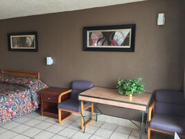 A hotel room with a bed, two chairs, a small table, and two framed pictures on the wall.