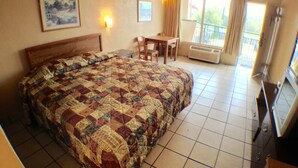 Une chambre d’hôtel avec un grand lit, un bureau, une chaise, une télévision et un balcon donnant sur l’extérieur.