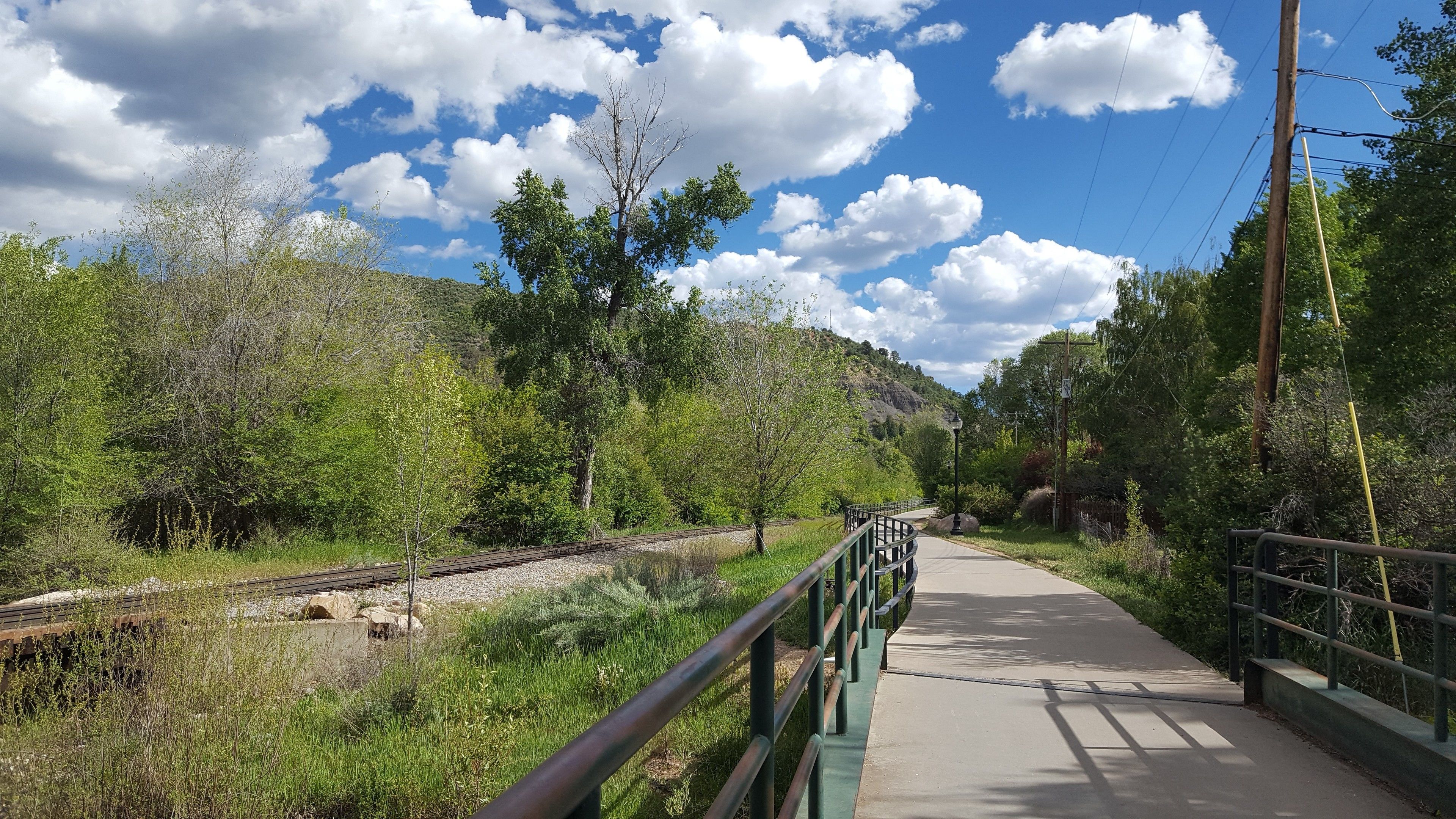 A pedestrian bridge with a metal railing, a concrete path, and a railway track alongside.