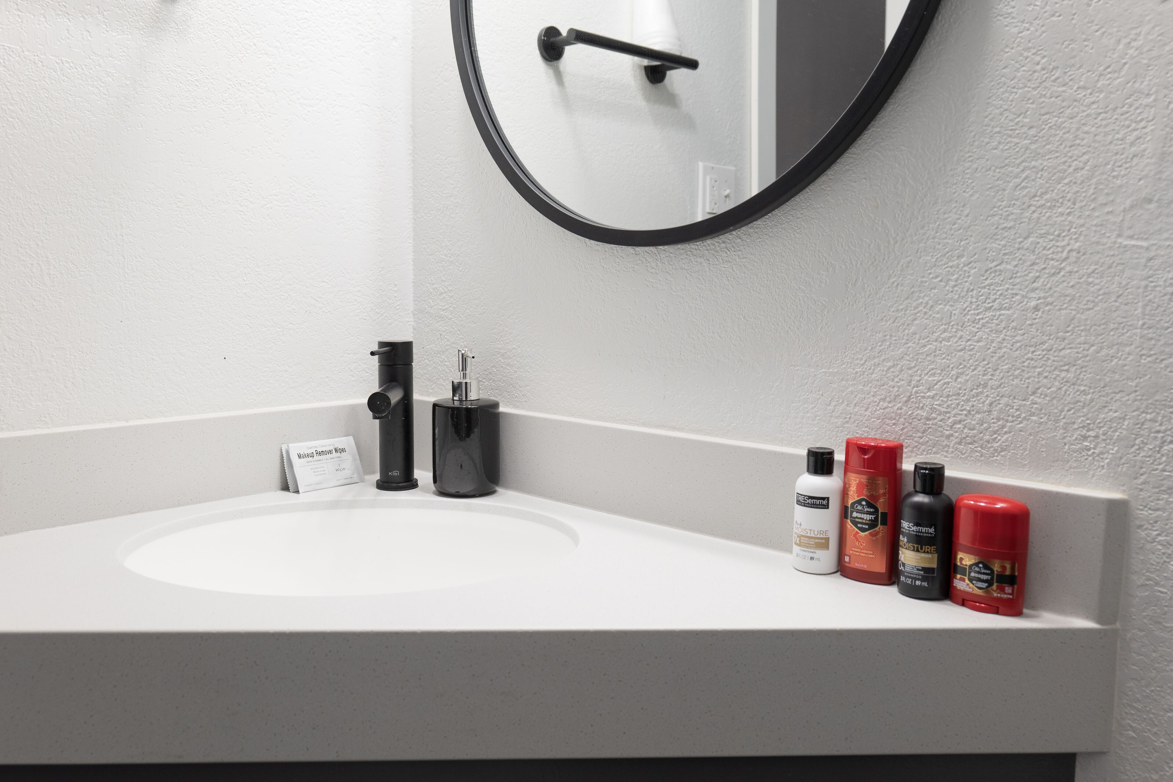 Une salle de bain avec un lavabo blanc, un miroir et quatre articles de toilette posés sur le comptoir.
