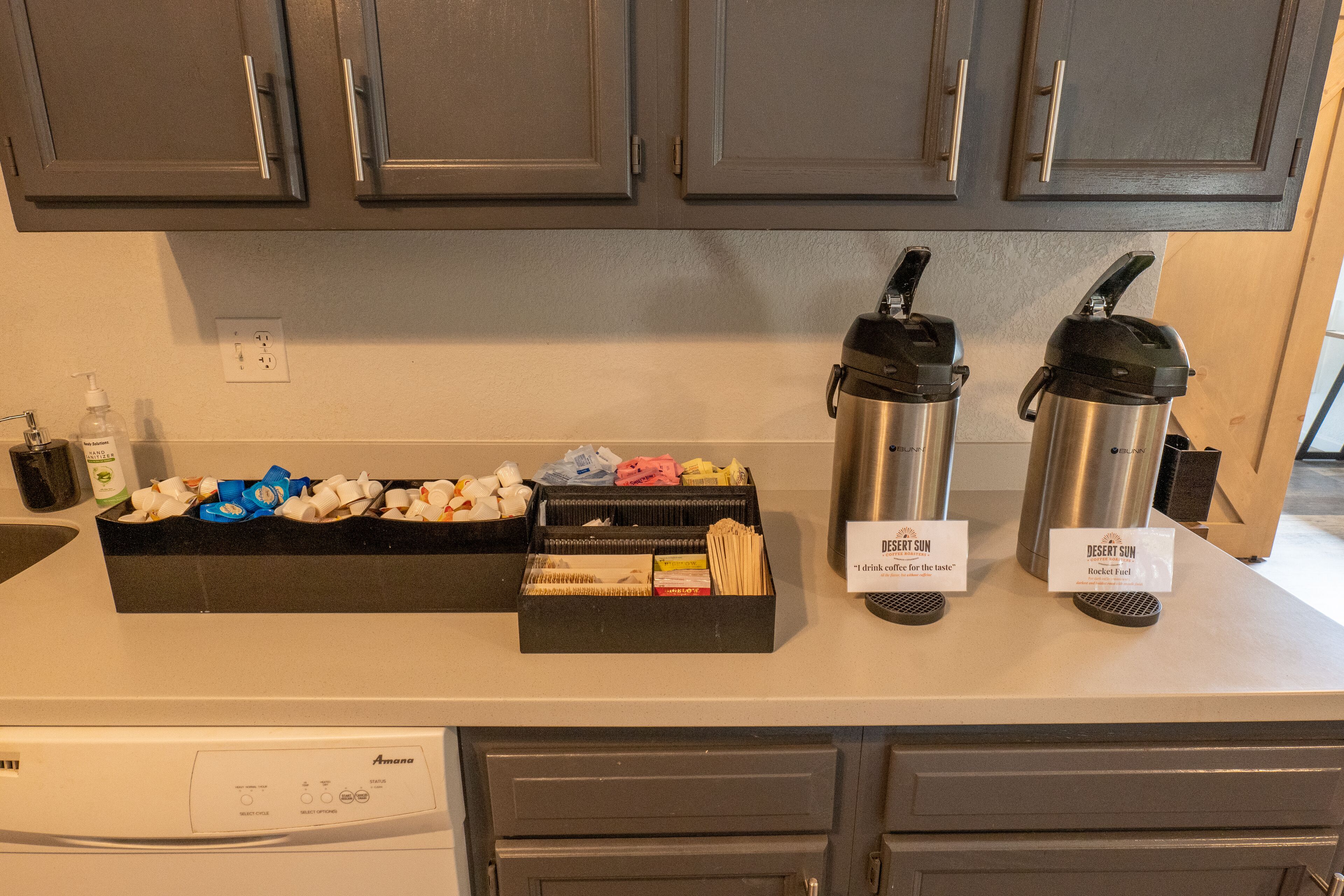 A kitchen counter with a coffee maker, two insulated water bottles, and a box of tea bags.