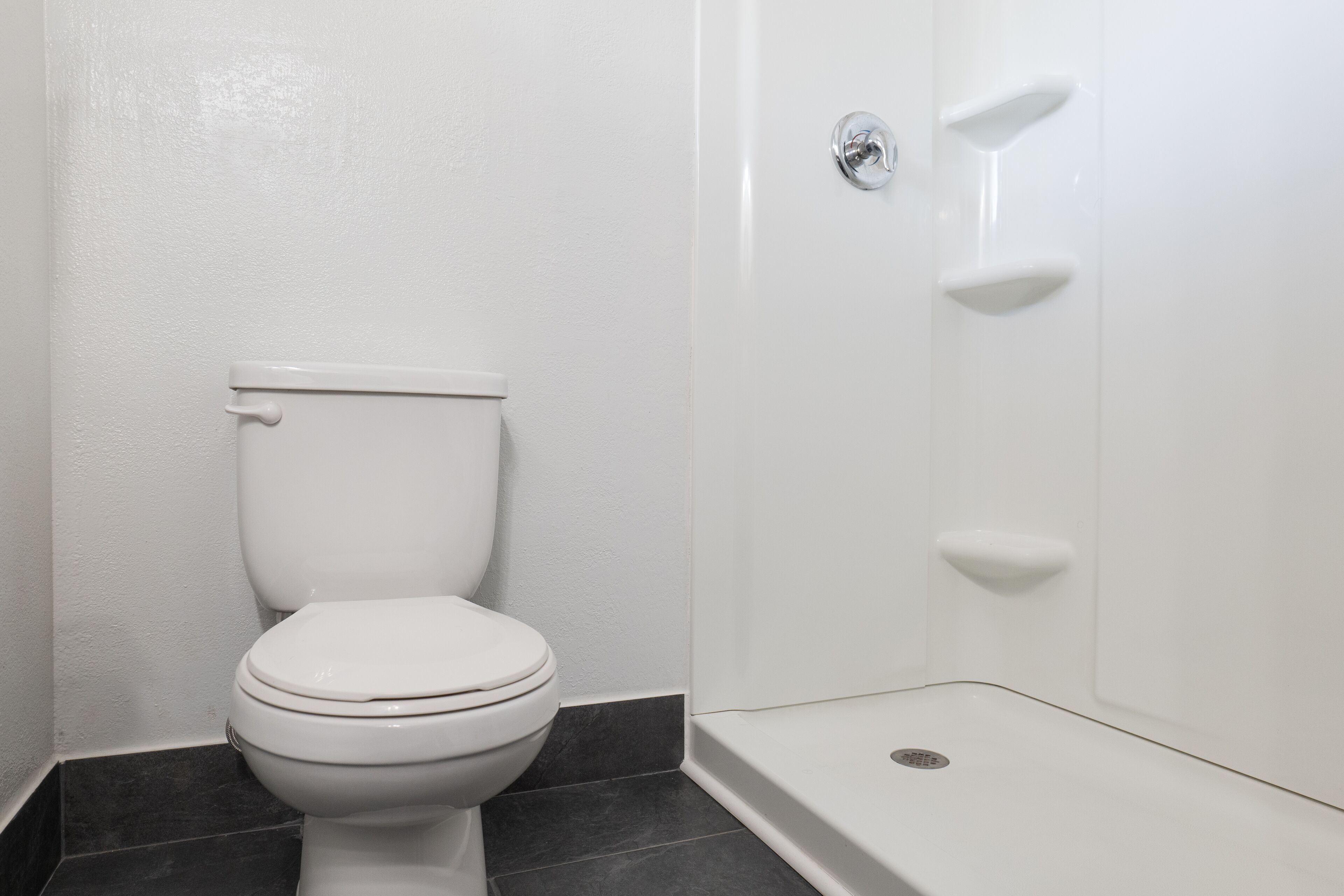 A bathroom with a white toilet, dark tiled floor, and white walls.