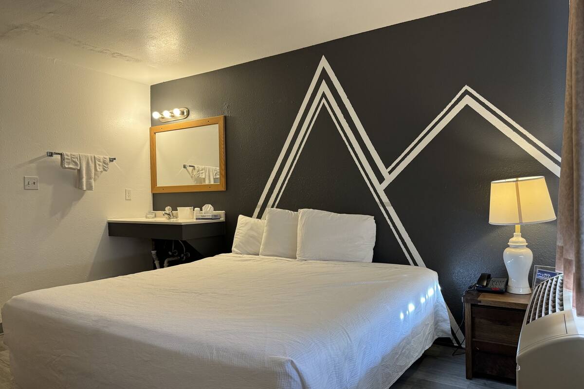 Une chambre d’hôtel avec un grand lit, une table de chevet avec une lampe, un miroir, un lavabo et un porte-serviettes.