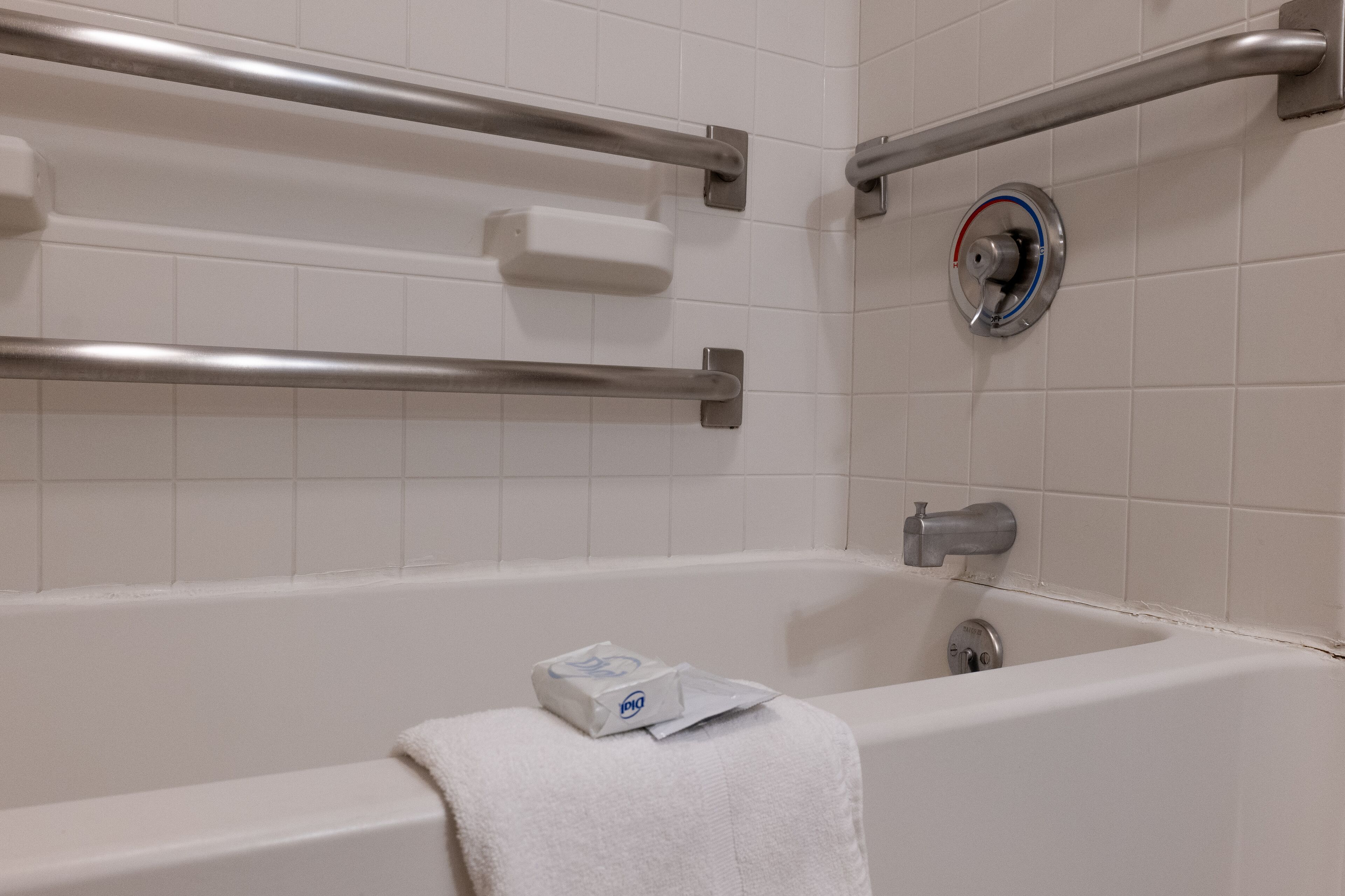 Ein Badezimmer mit einer Badewanne, Haltegriffen, einem Handtuch und einer Seifenspender.