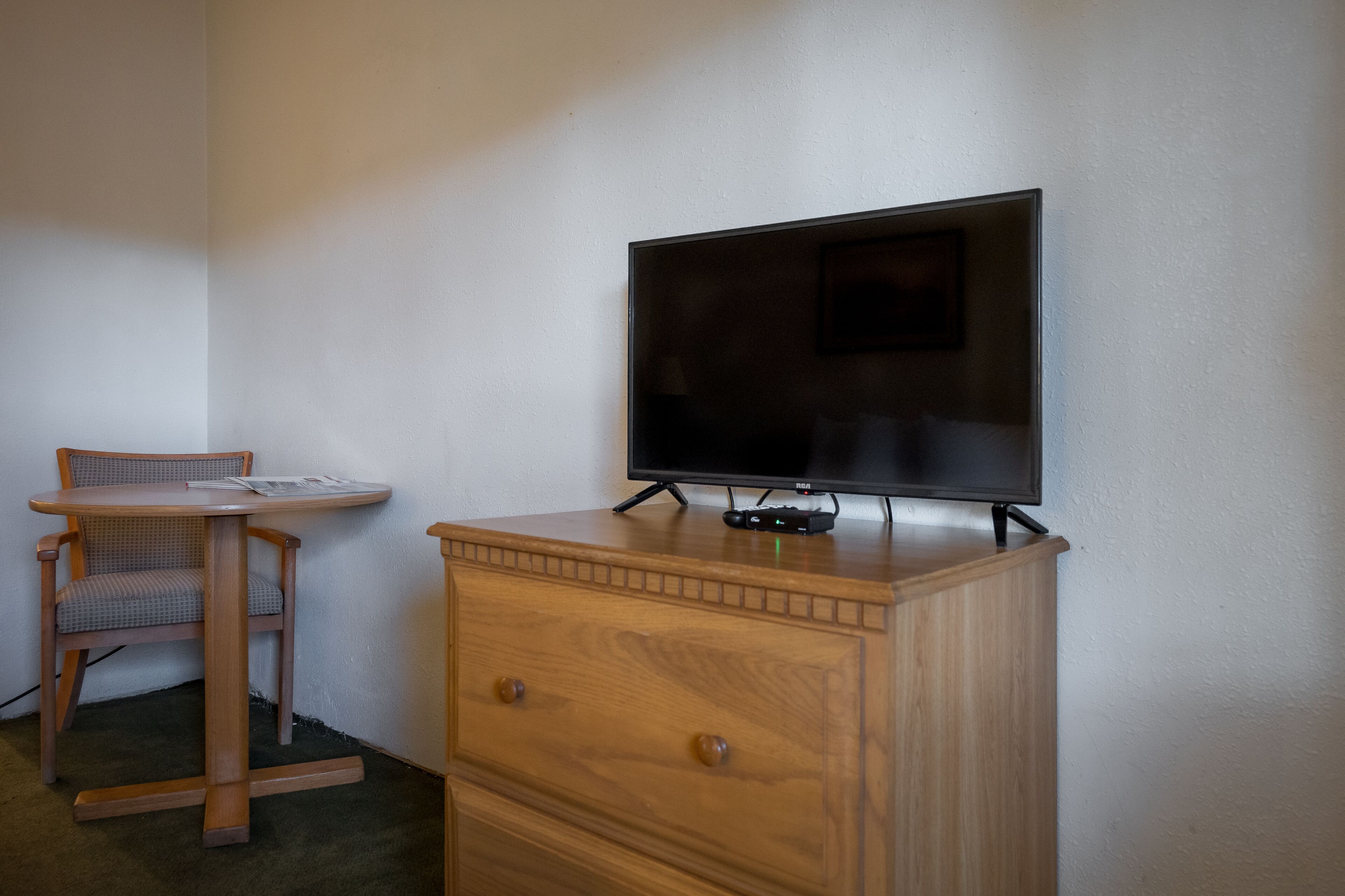 Een houten dressoir met een flatscreen televisie erop, een kleine houten stoel en een tafeltje met een tijdschrift.