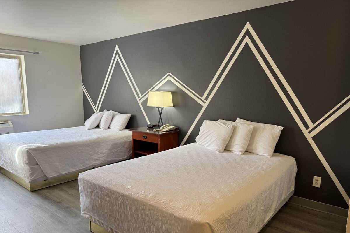 Une chambre d’hôtel avec deux lits, une table de chevet avec une lampe et un motif géométrique sur le mur.