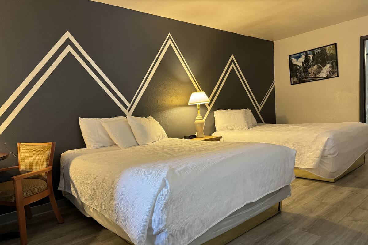 Une chambre d’hôtel avec deux lits, une chaise, une table de chevet et un tableau accroché au mur.