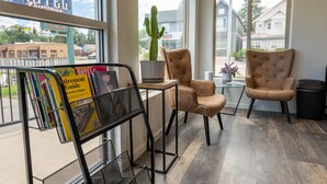 Une chambre d’hôtel avec une grande fenêtre, un cactus, deux fauteuils, une petite table et un porte-revues.