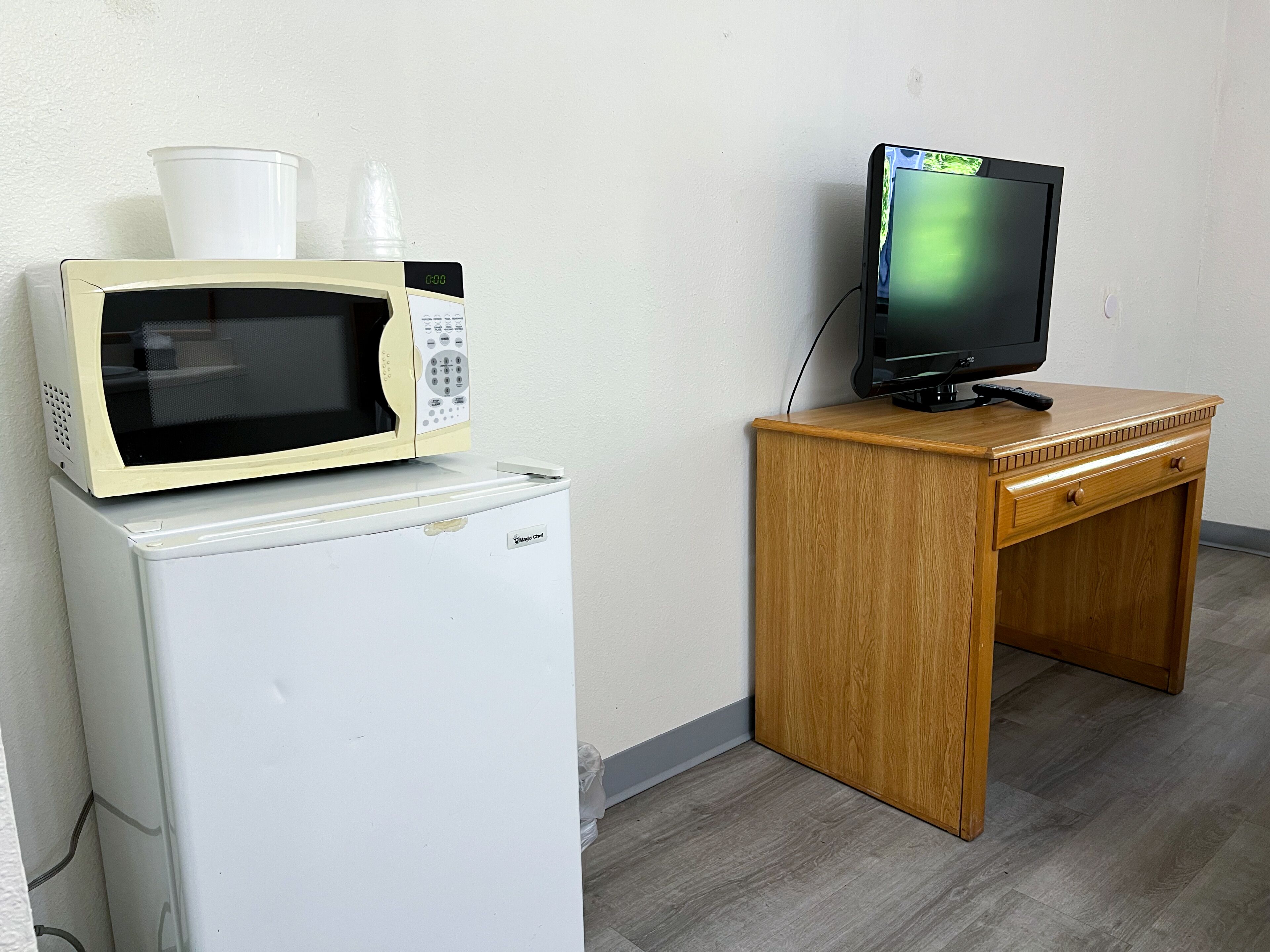 Una kitchenette compacta con microondas, refrigerador y un escritorio de madera con televisor.