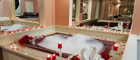 A spa room with a large bathtub, mirrors, and rose petals.