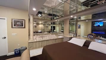 A hotel room with a large bed, a bathroom with a glass-enclosed shower, a television, and a framed picture on the wall.