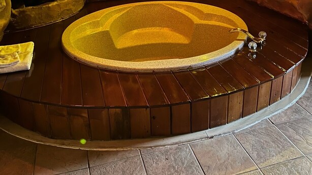 A spa area with a hot tub, wooden flooring, and a rock wall with plants.