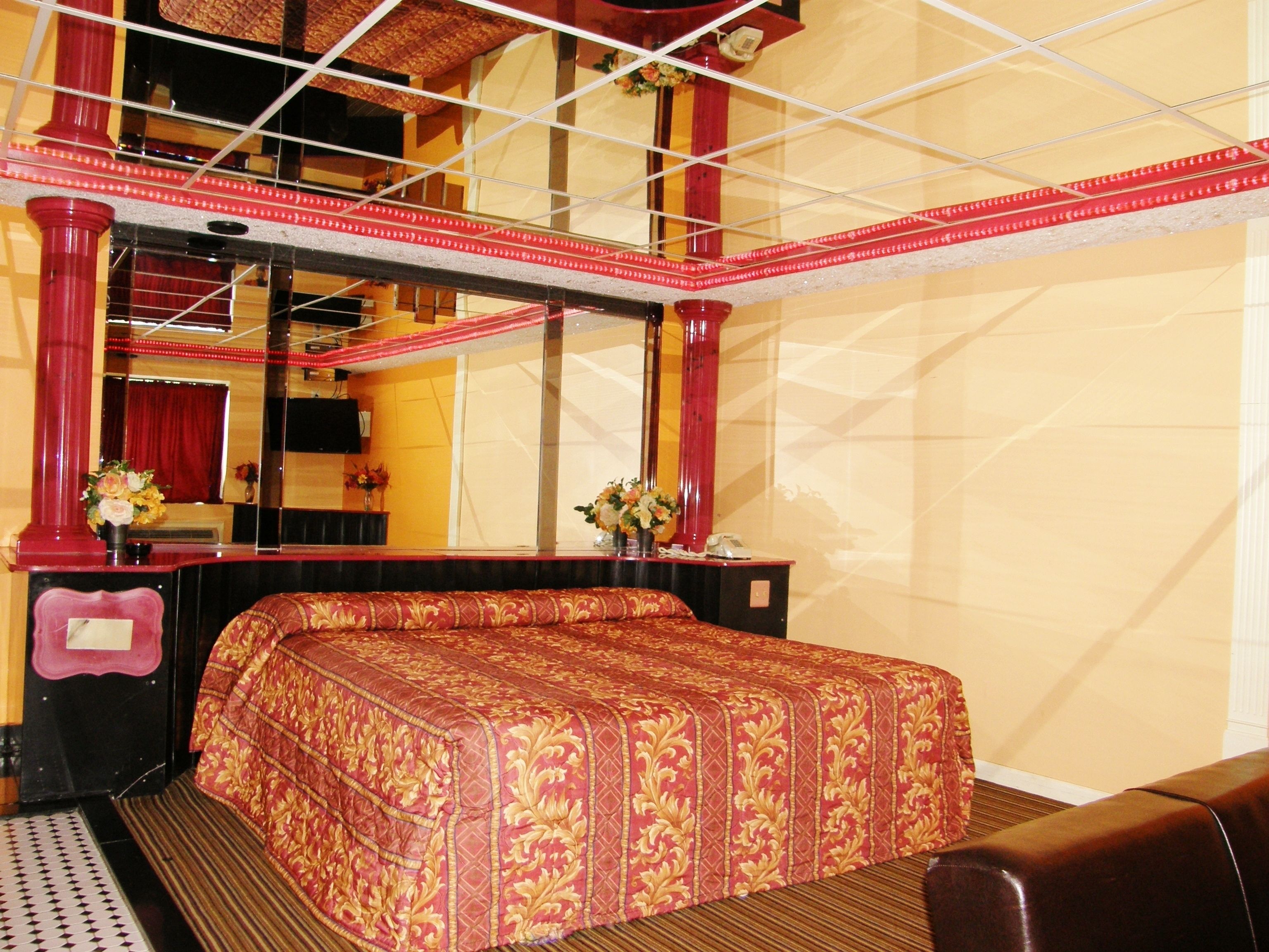 A hotel room with a large bed, a sitting area, a mirror, and a red decorative railing.