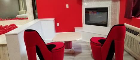 A modern kitchen with red walls, a white countertop, and a built-in oven. There are two red chairs with black accents and a small round table.