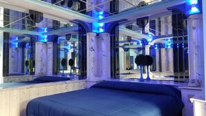 A modern hotel room with a large bed, multiple mirrors, and blue lighting accents.