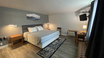 A bedroom with a bed, bedside tables, a desk, a chair, a TV, and a patterned rug.
