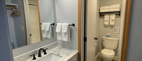 A modern bathroom with a marble sink, a large mirror, and a toilet visible through an open door.