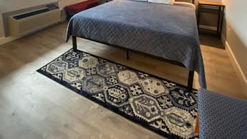A bedroom with a bed, a patterned rug, a nightstand, a wall-mounted artwork, and a window with curtains.