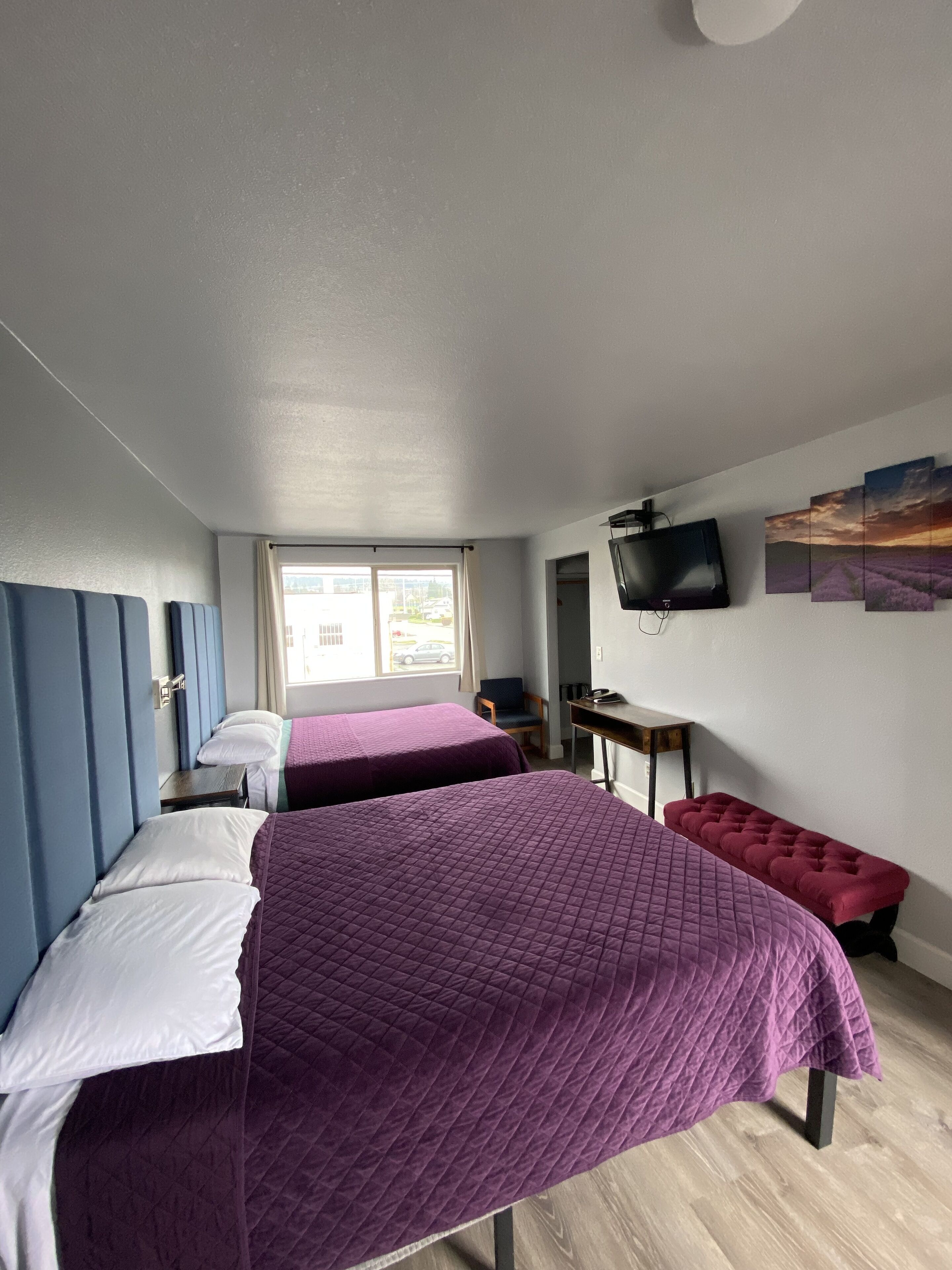 A room with two beds, a desk, a chair, a television, and a window with a view of the outside.