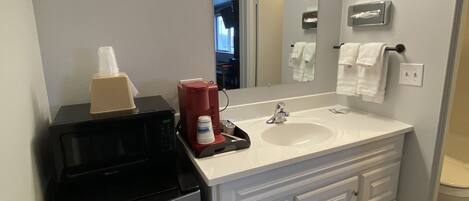 A bathroom with a double sink, a mirror, a coffee maker, and a refrigerator.