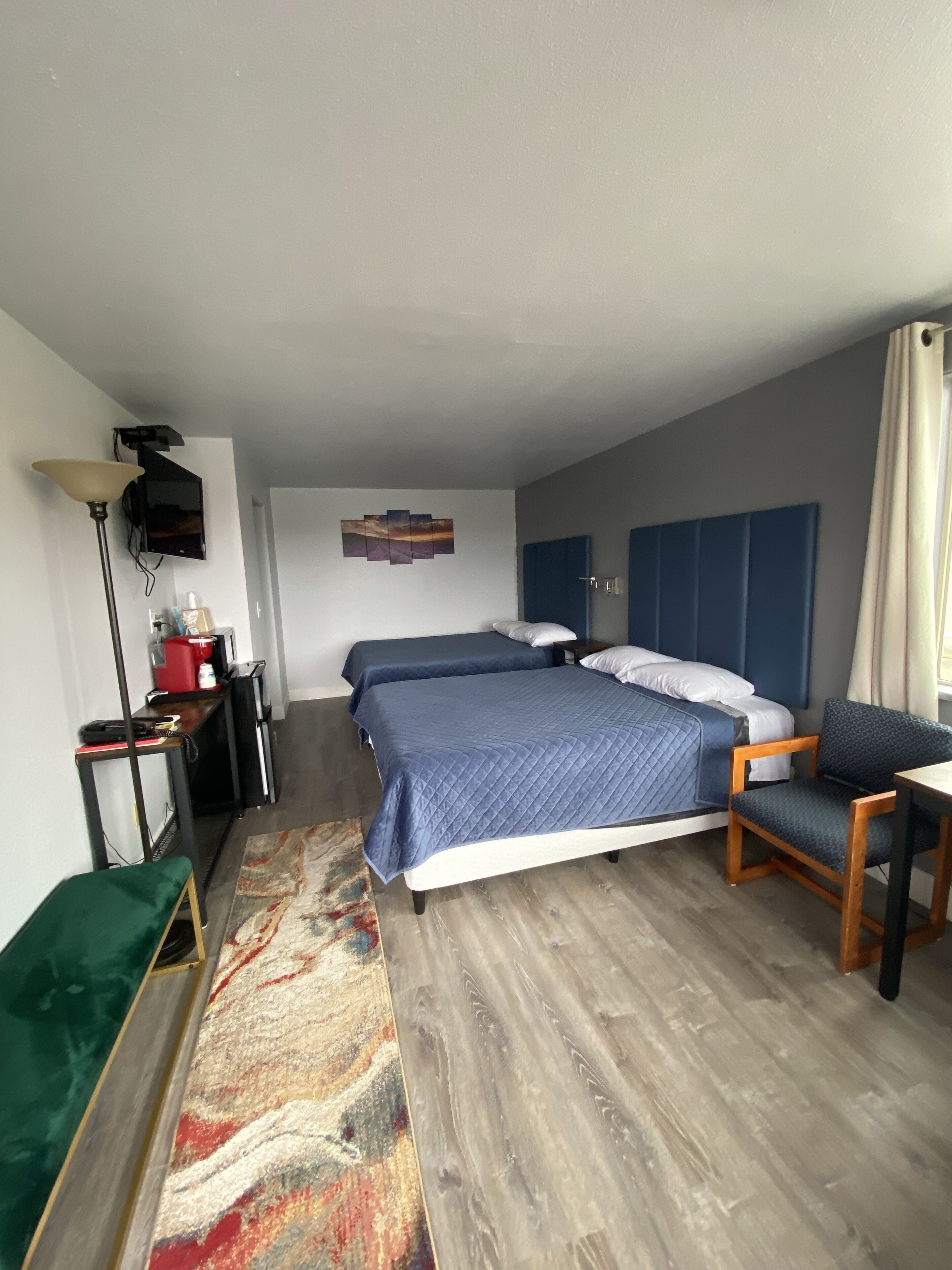 Une chambre d’hôtel avec deux lits, un bureau, une chaise, une lampe et un téléviseur.