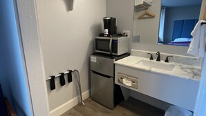 Ein kompaktes Hotelzimmer mit Küchenzeile, einer integrierten Mikrowelle, einem kleinen Kühlschrank, einem Spülbecken und einem Spiegel.