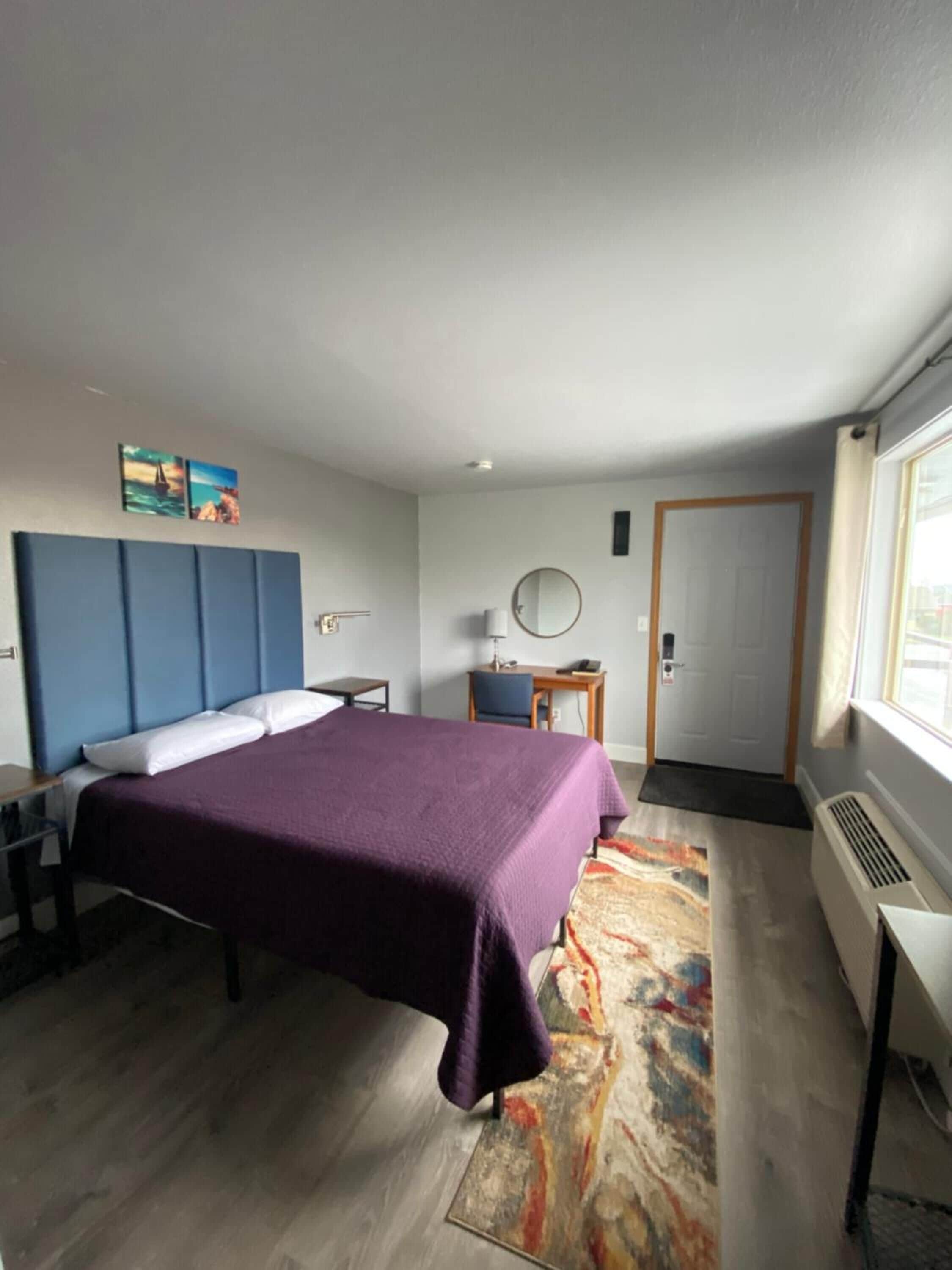 Una habitación de hotel moderna con una cama grande, un escritorio, una silla, una mesita, un espejo y una puerta.