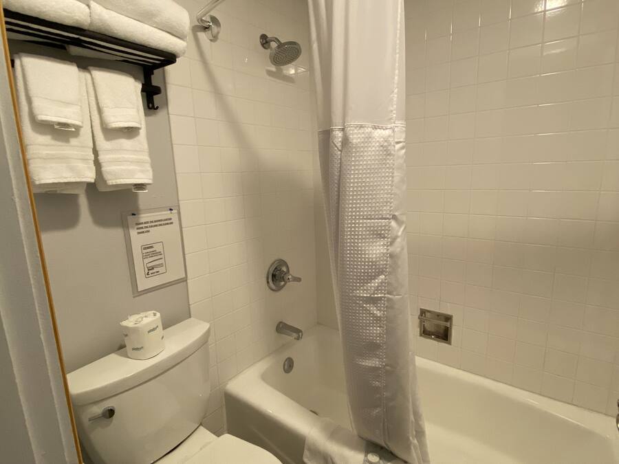 Une salle de bain avec des toilettes, une douche avec un rideau blanc et un porte-serviettes avec des serviettes pliées.