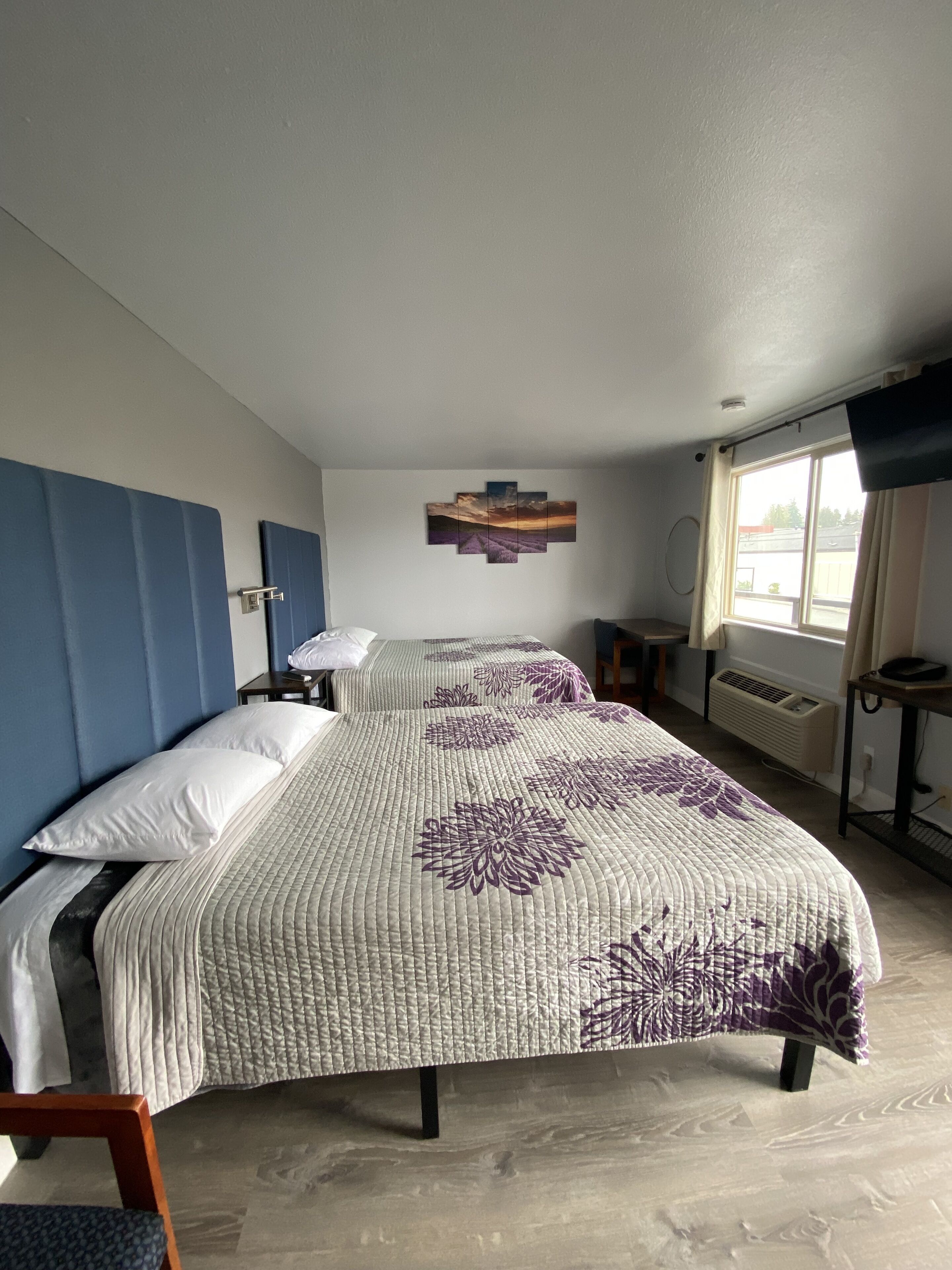 Hotelkamer met twee bedden, een flatscreen televisie, een raam met gordijnen en een wanddecoratie.