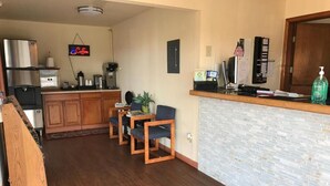 Eine Küche mit Holzausstattung, einer Kaffeemaschine und einem Kühlschrank. Es gibt einen Essbereich mit zwei Stühlen und einem Tisch.