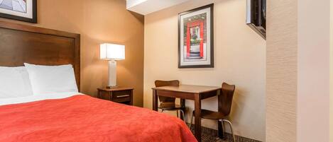 A hotel room with a large bed, a desk with two chairs, a lamp, and a framed picture on the wall.