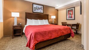 A hotel room with a large bed, two bedside tables with lamps, a desk with chairs, and framed pictures on the walls. - Rodeway Inn Chicago - Evanston (Chicago)