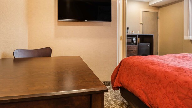A hotel room with a bed, a TV mounted on the wall, a desk, and a chair. - Rodeway Inn Chicago - Evanston (Chicago)