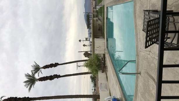 A pool area with a view of the beach, palm trees, and a covered seating area. - Western Sands Motel (Indio)