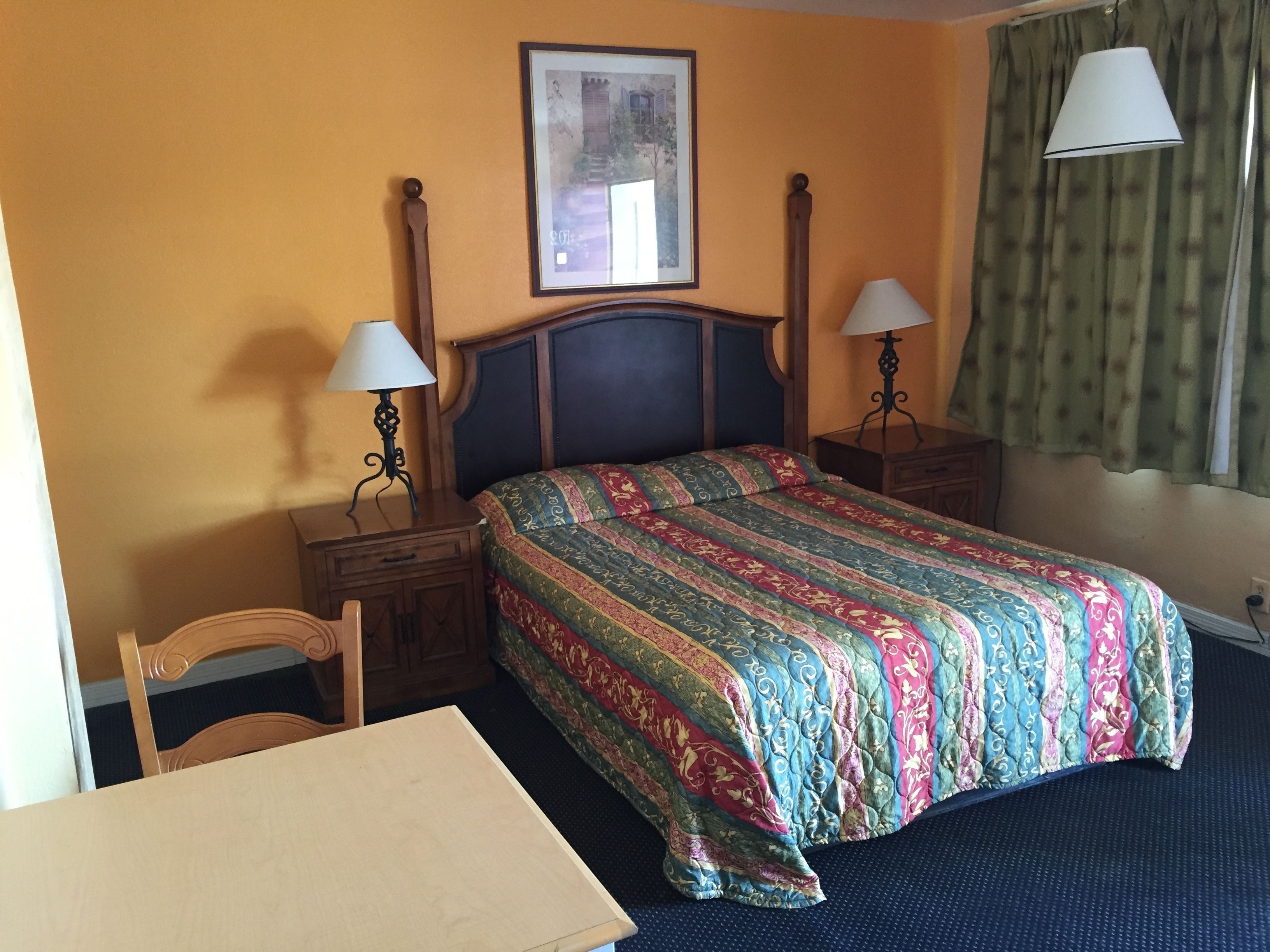 A hotel room with a bed, two bedside tables with lamps, a chair, a desk, and a framed picture on the wall.