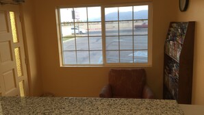 A room with a large window, a chair, and a bookshelf. - Western Sands Motel (Indio)