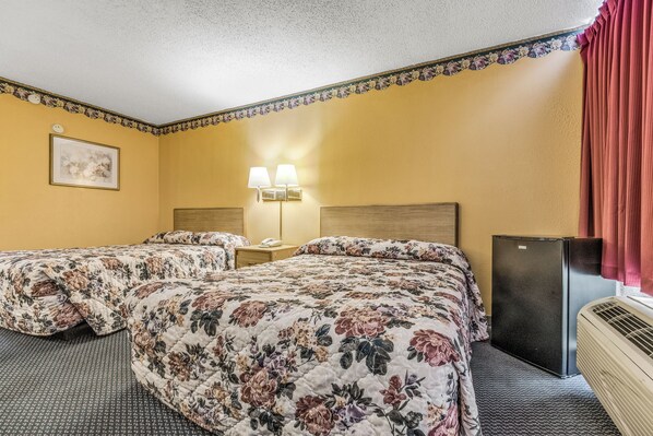 A hotel room with two beds, a nightstand with lamps, a refrigerator, and a window with curtains.