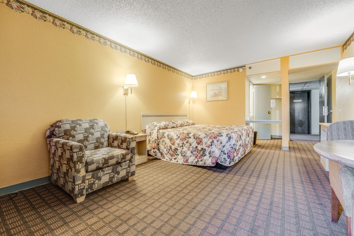 Una habitación de hotel con un sillón estampado, una cama con ropa de cama floral y una mesita de noche con una lámpara.