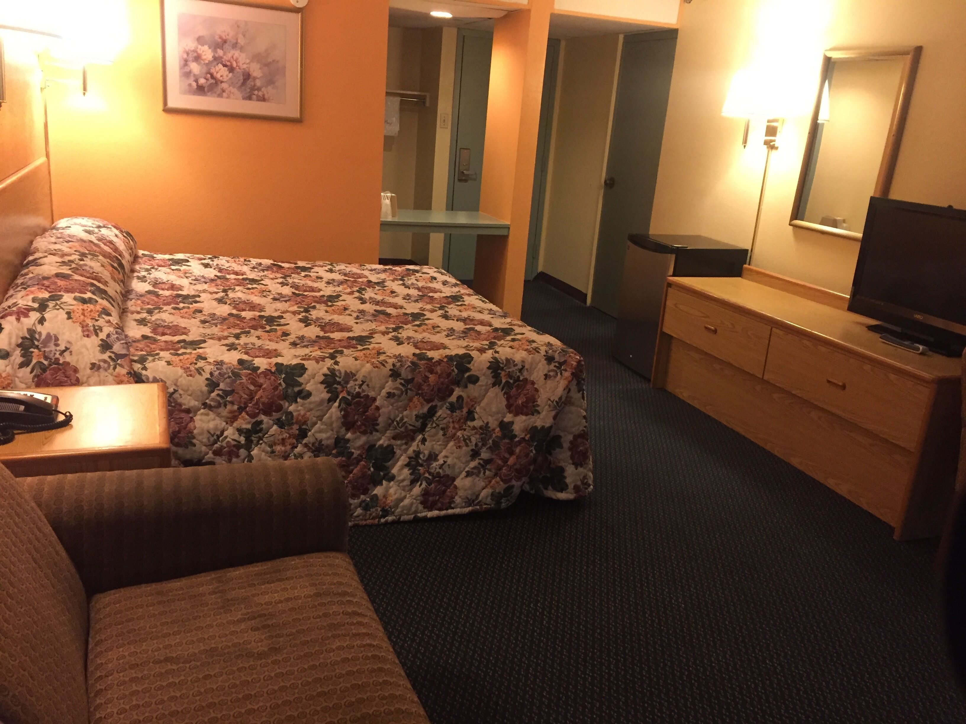 Habitación de hotel con cama, escritorio, cómoda, televisor y baño visible a través de una puerta abierta.