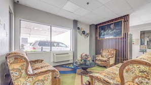Een kamer met gestreepten banken, een houten stoel, een ronde tafel met een vaas, en een groot raam met uitzicht op geparkeerde auto's.