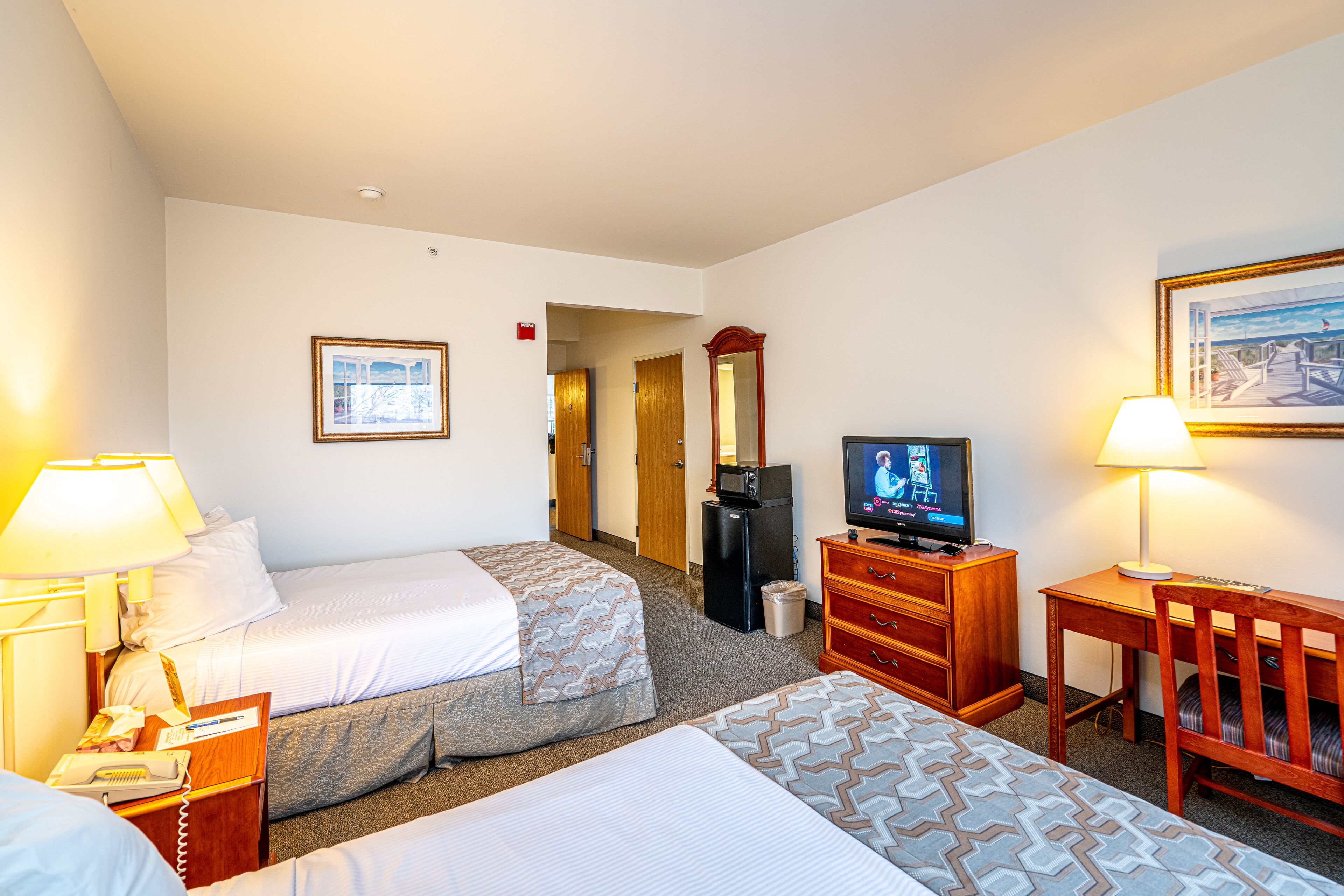 Een hotelkamer met twee bedden, een televisie, een bureau, een stoel, een lamp en een lijst met een foto aan de muur.