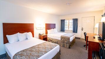 A hotel room with two beds, a desk with a computer, a TV, and a window with curtains.