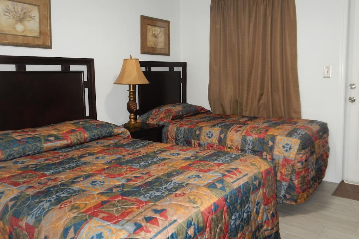 A room with two beds, a nightstand with a lamp, and a door.