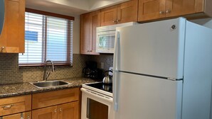 Una cocina con armarios de madera, un lavamanos de acero inoxidable, un horno empotrado, un refrigerador blanco y un microondas.