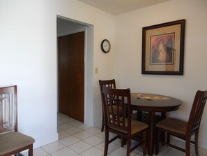 A dining area with a round table, two wooden chairs, a clock, and a framed picture on the wall. - Shell Motel (Hollywood)
