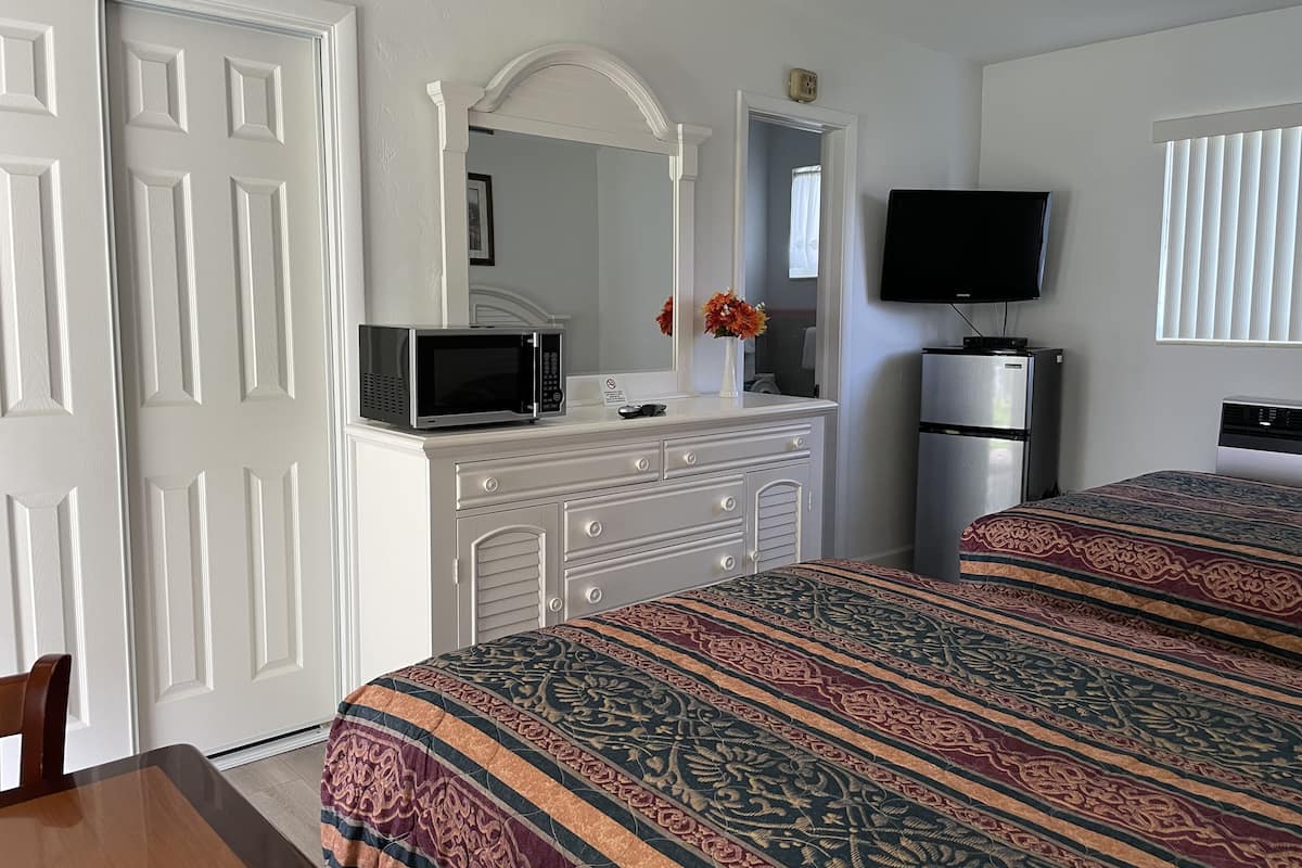 A hotel room with a bed, a dresser, a microwave, a television, and a refrigerator.