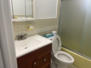 A bathroom with a white sink, a mirror above it, a toilet with a closed lid, and a shower area with a glass door. - Shell Motel (Hollywood)