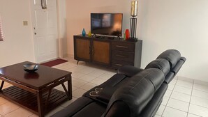 Una sala de estar con un sofá, un televisor sobre un mueble bajo y una puerta.
